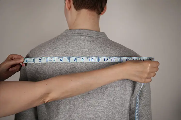 Man standing in a grey jumper being measured.